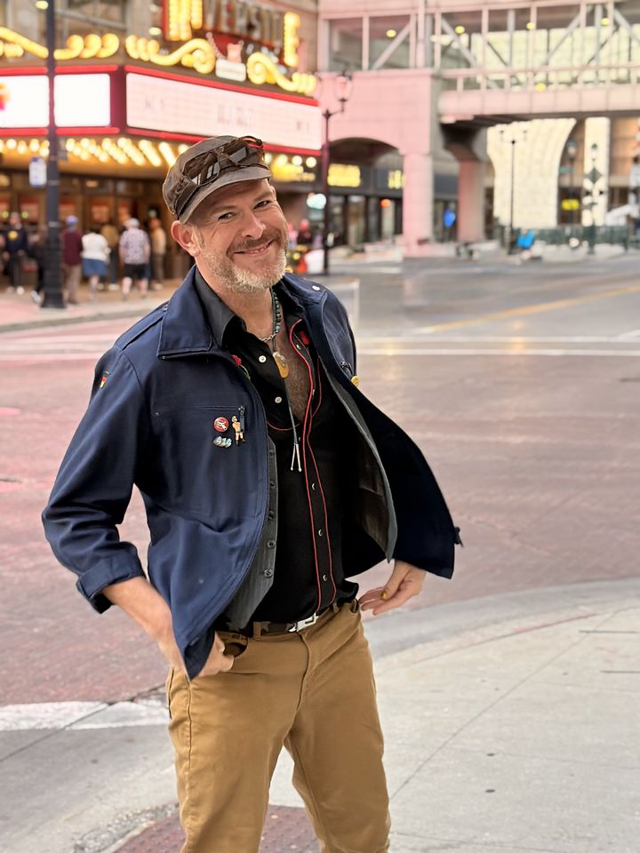 Aaron Berth, smiling on a downtown Milwaukee corner in a newsboy cap and navy jacket