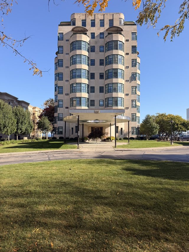 The Exton, a cream Art Deco apartment tower with curved corner windows and a round entrance canopy, over a wide lawn.