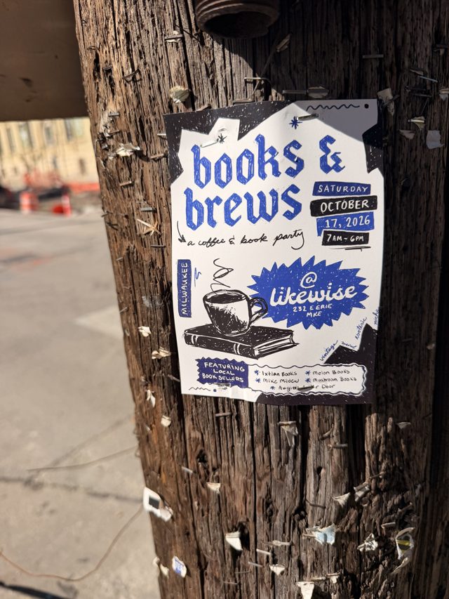 A blue Books & Brews poster stapled to a telephone pole thick with old staples, a street of orange construction barrels behind it.