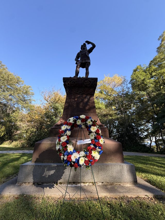 The Leif Erikson statue on a tall granite base, shading his eyes, a red, white and blue wreath at its foot.