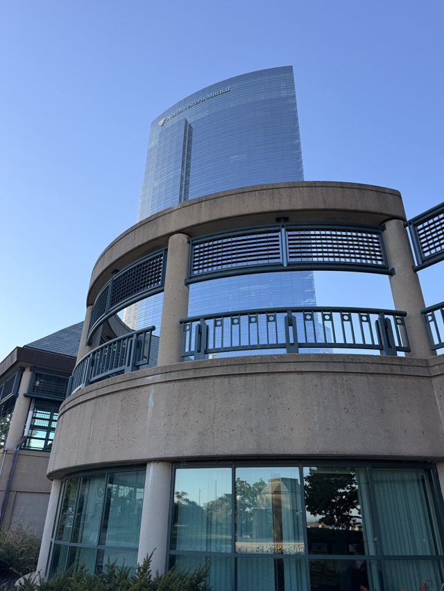 The curved glass Northwestern Mutual tower rising behind a round concrete stair with green railings.