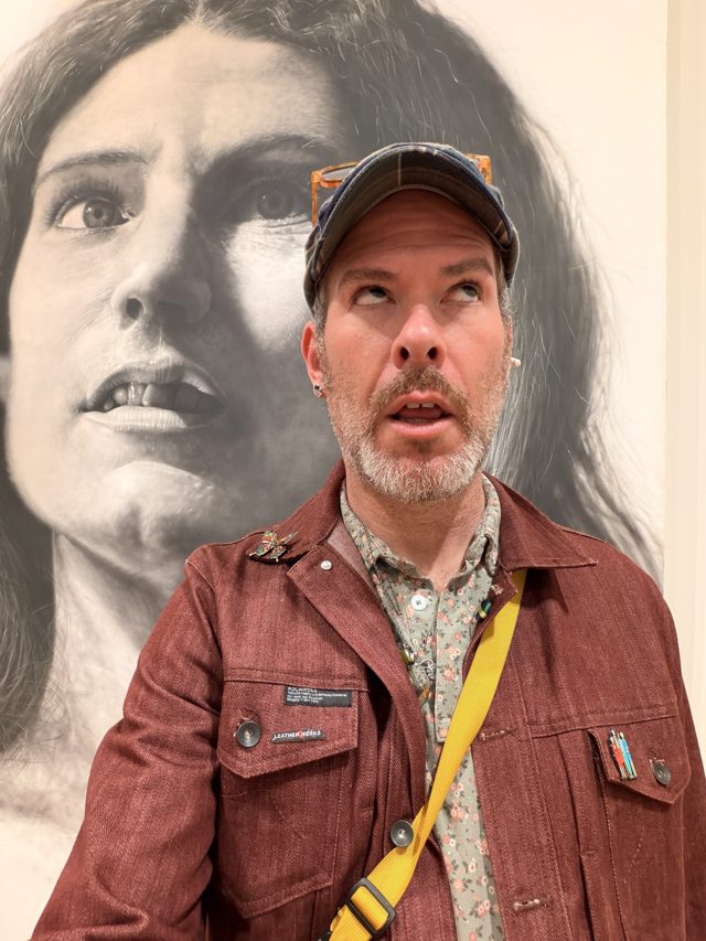 Aaron looking up, mouth open, under an enormous black-and-white painted portrait.