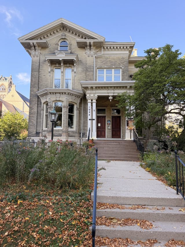A cream-brick Italianate house with a columned porch at the top of a long flight of steps, leaves on the walk.