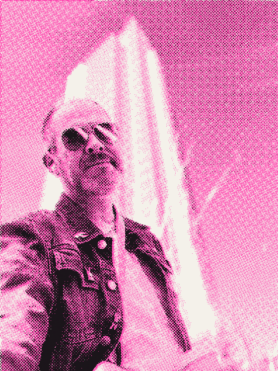 Aaron in sunglasses and a denim jacket, looking up from the foot of a glass office tower