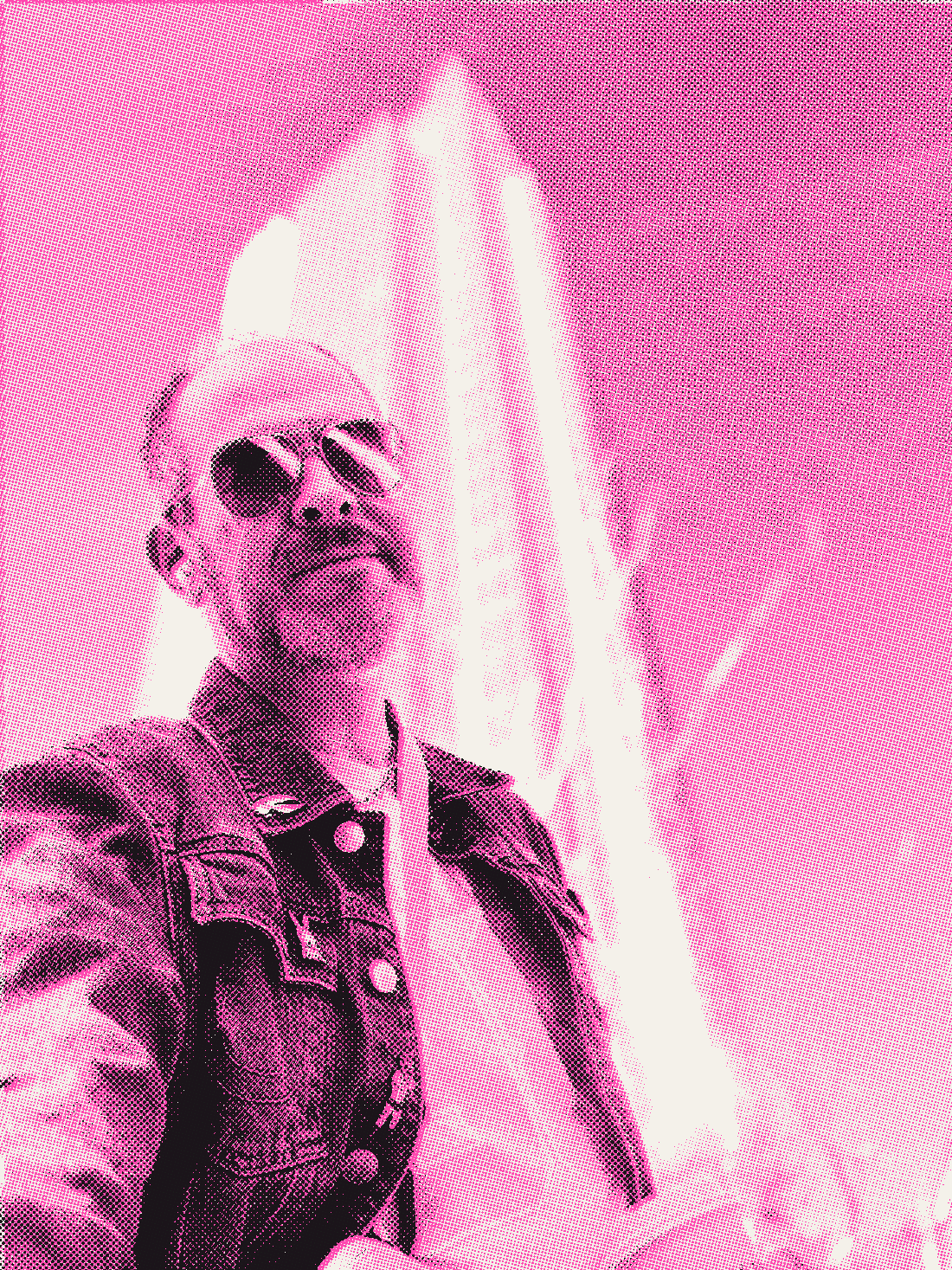 Aaron in sunglasses and a denim jacket, looking up from the foot of a glass office tower