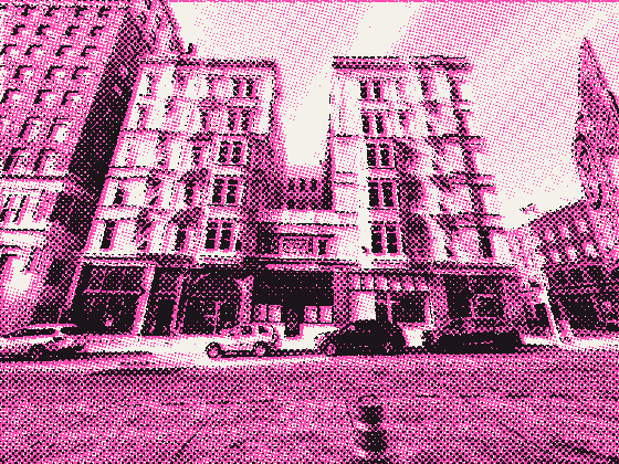Two old stone apartment buildings behind a closed street and an orange traffic barrel