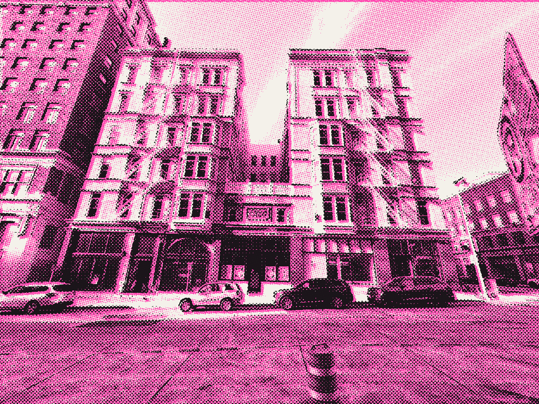 Two old stone apartment buildings behind a closed street and an orange traffic barrel