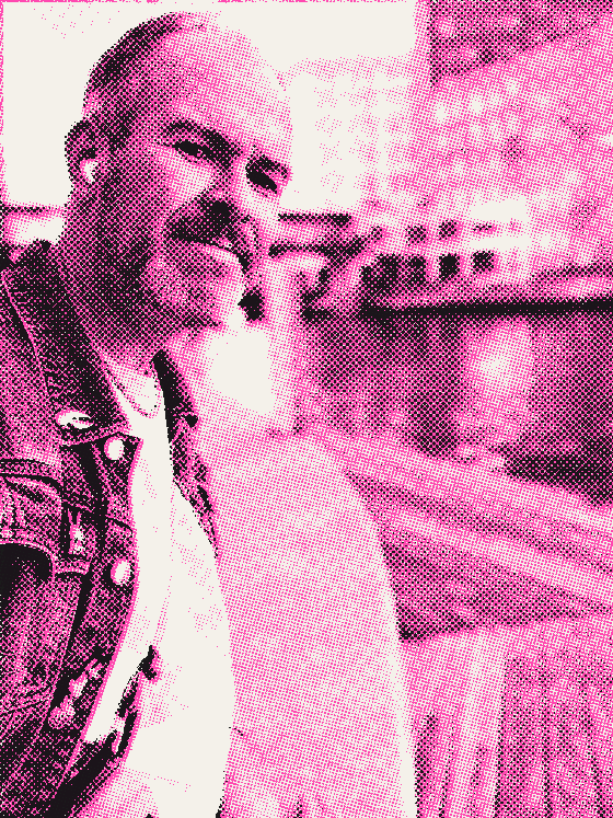 Aaron at the river's edge, half smiling, buildings soft behind him