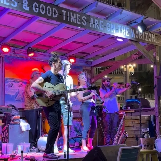 The band on stage at Sunset Pier under a Good Times Are On The Horizon sign
