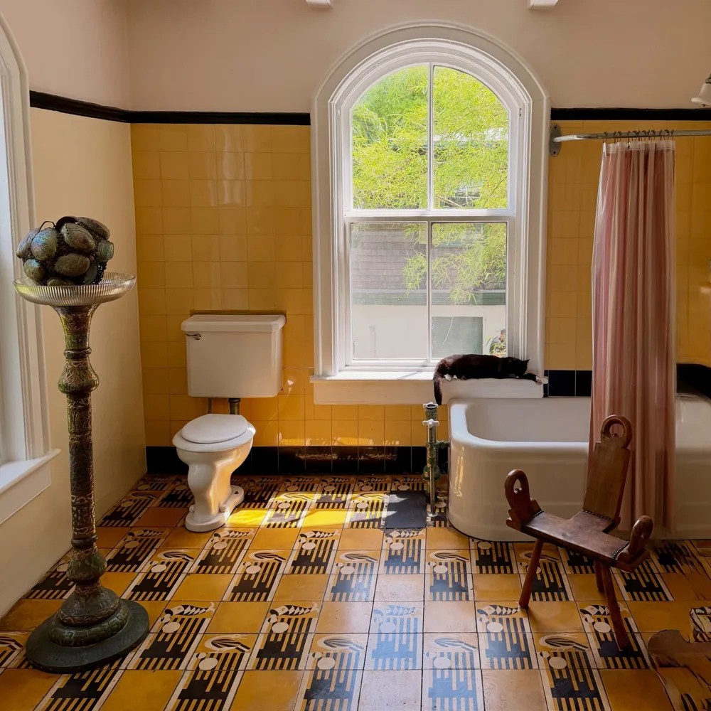 Hemingway's yellow-tiled bathroom with a claw-foot tub and a cat on the windowsill