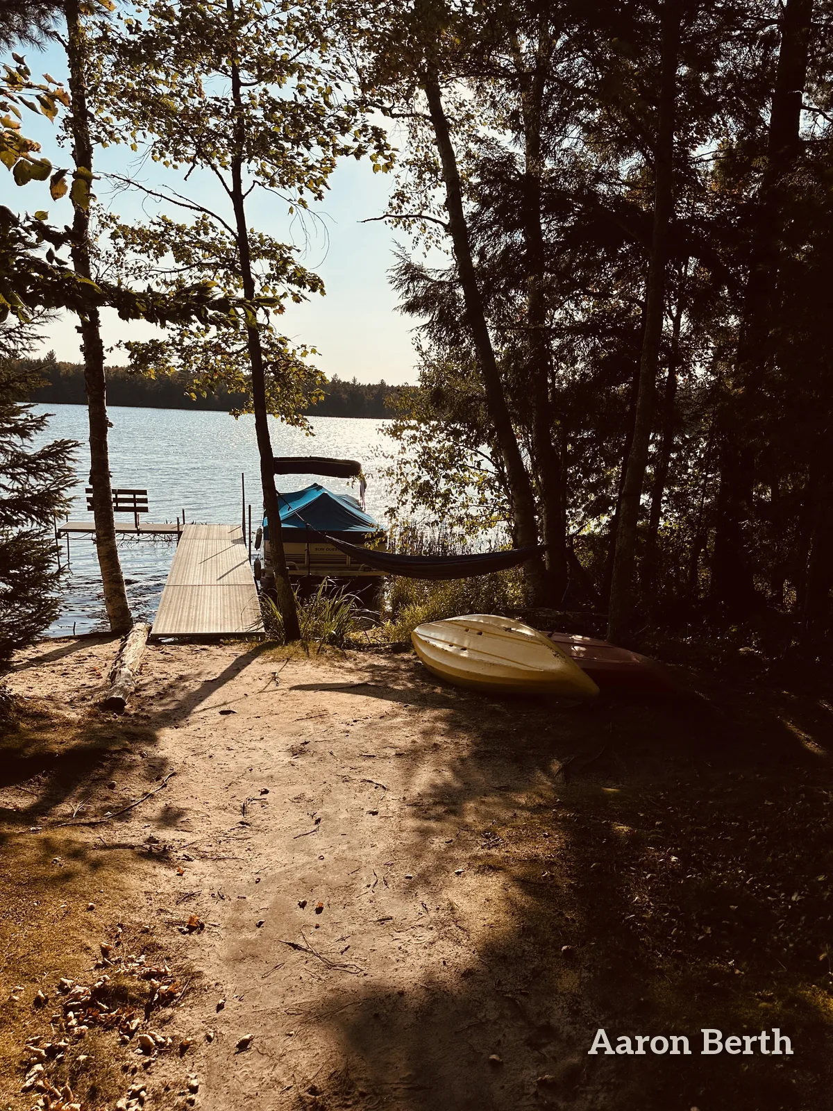 A lake dock, a boat and a hammock through north-woods trees in September light, no one in frame