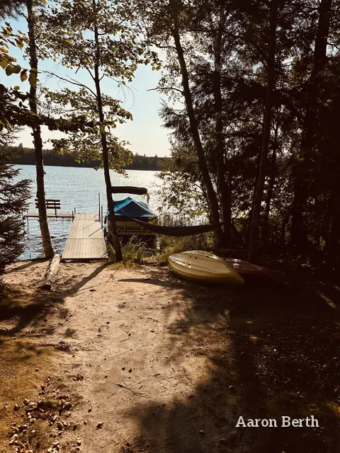 A lake dock, a boat and a hammock through north-woods trees in September light, no one in frame