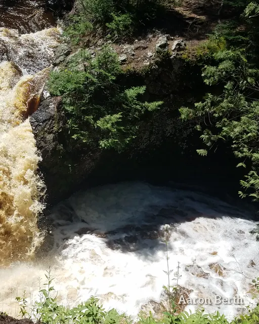 A tannin-brown waterfall plunging into a rocky pool