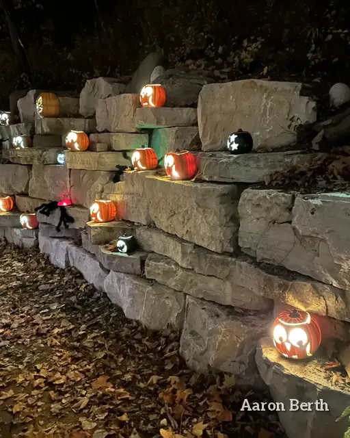 Rows of lit jack-o-lanterns on stone steps in a dark autumn park