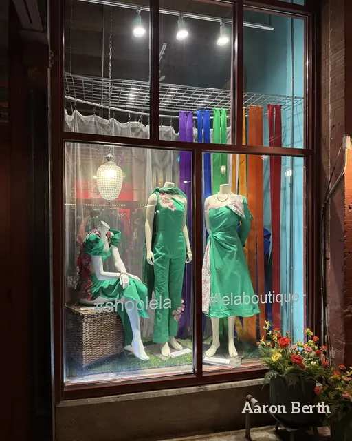 A lit shop window with two green dresses on mannequins at night