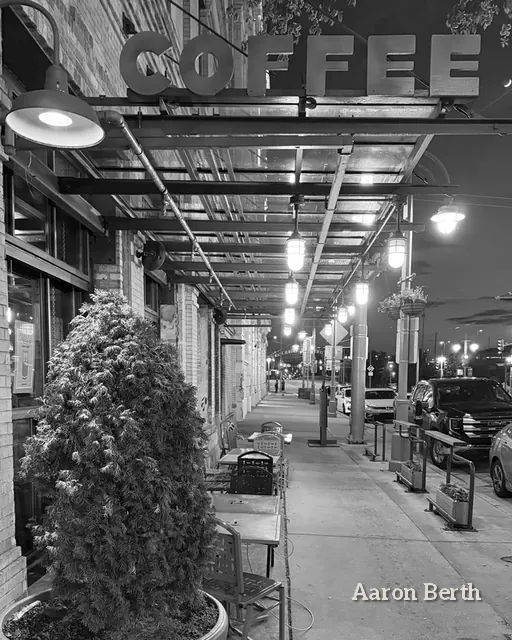 Black and white: a quiet street under a coffee shop sign, lights strung overhead