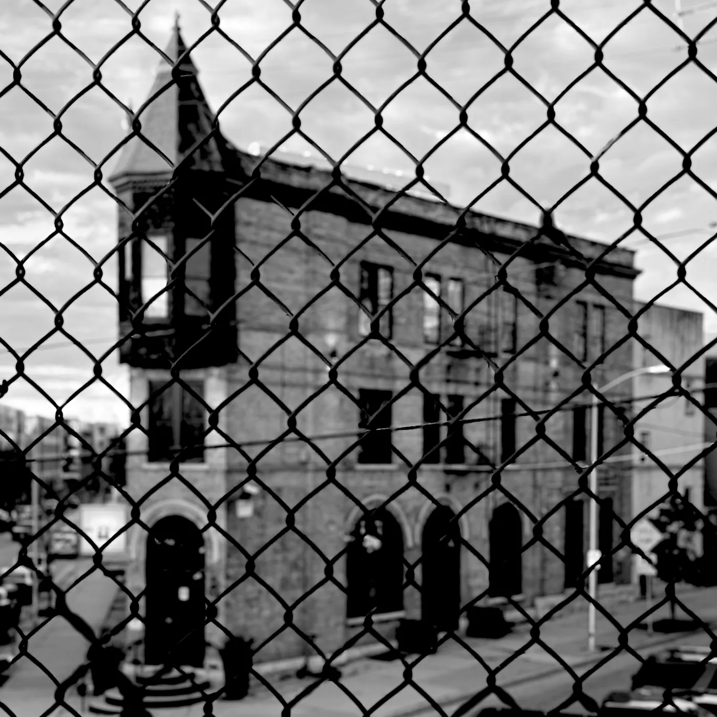 A turreted brick building seen through a chain-link fence, in black and white