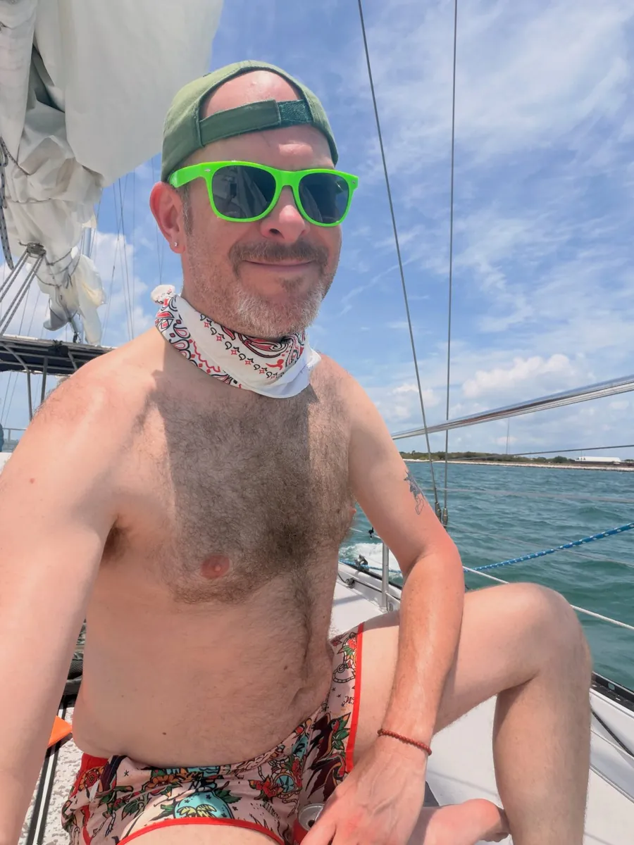 Aaron on the deck of the sailboat after his first snorkel, sunglasses on, open water behind