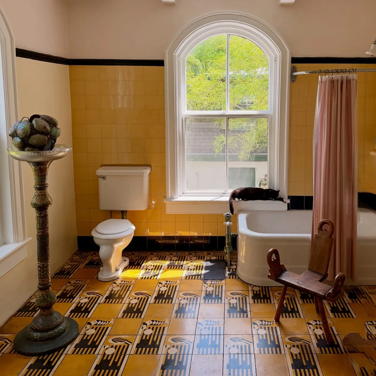 Hemingway's yellow-tiled bathroom with a claw-foot tub and a cat on the windowsill