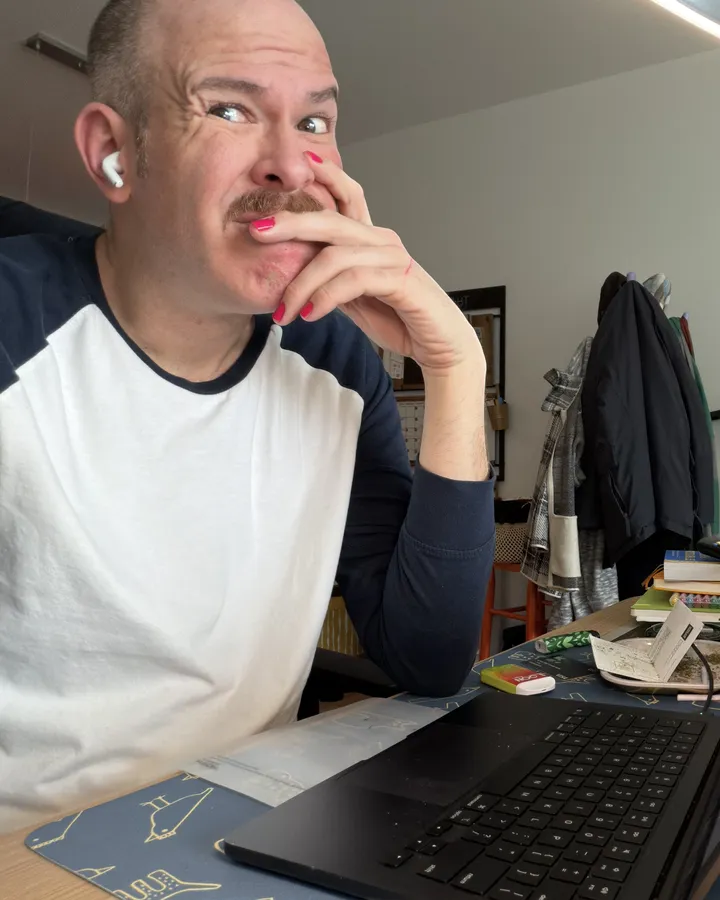 Aaron at his kitchen table in an earbud, laptop open, hand over his mouth, listening