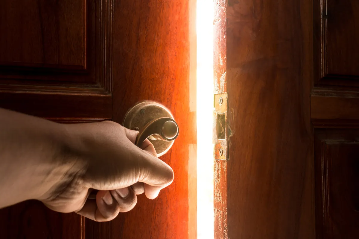 A hand opening a door onto bright light