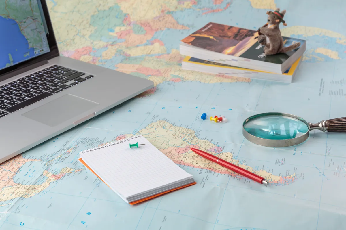A map, notepad and laptop laid out for trip planning