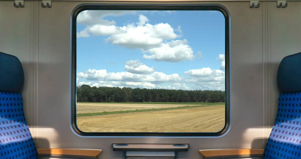 An empty train seat beside a window onto farm fields
